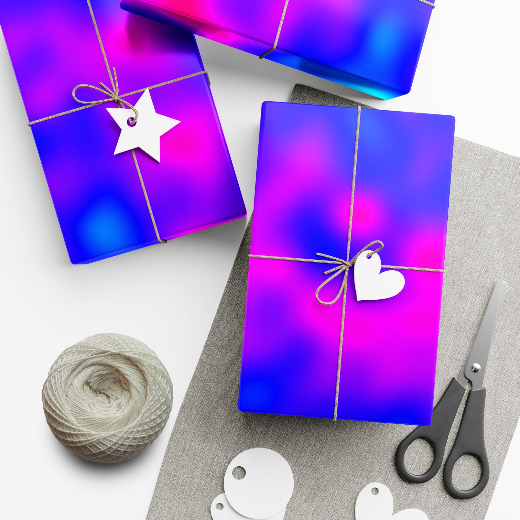 Two wrapped gifts with decorative tags on a white surface, accompanied by yarn and scissors.