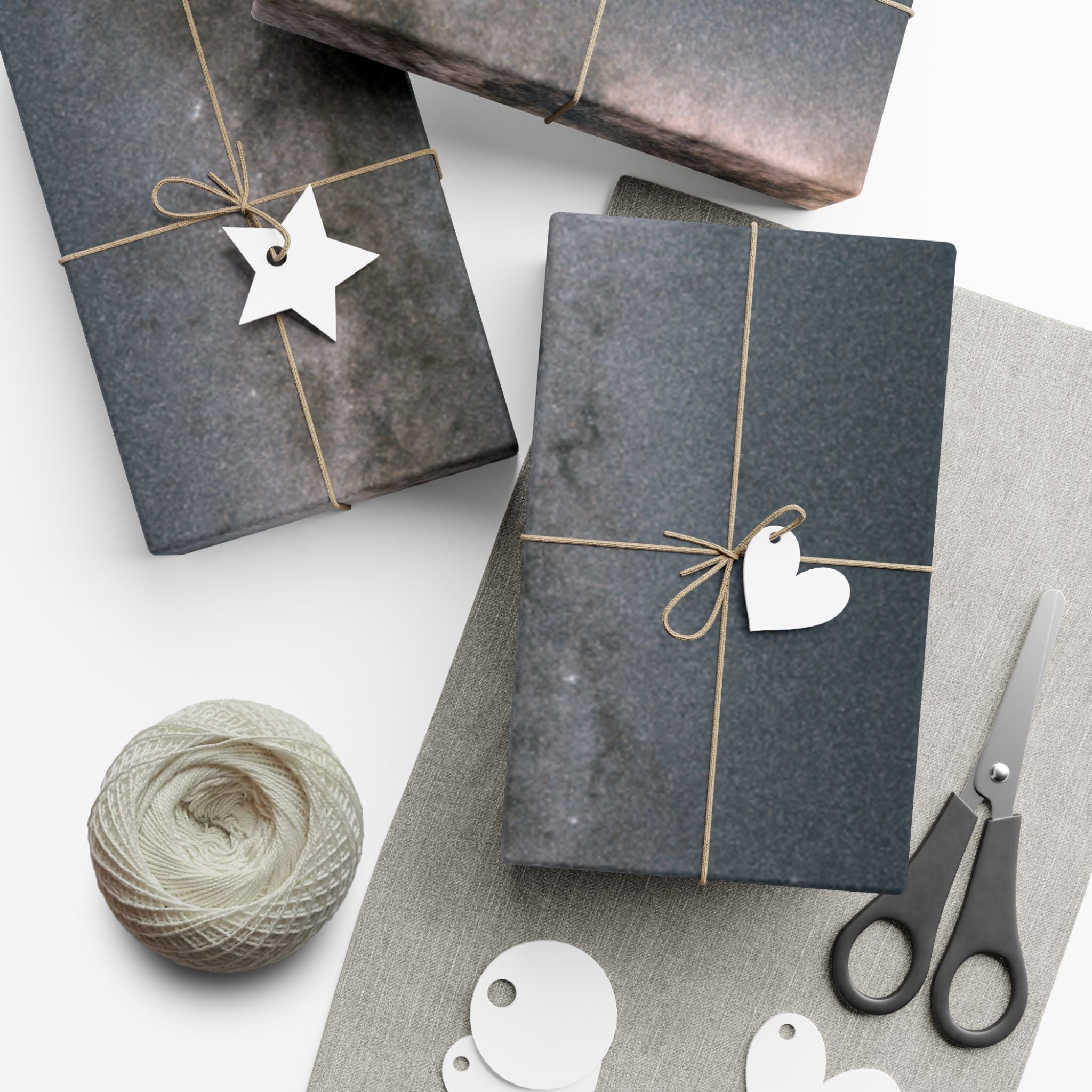 Gift boxes wrapped in galaxy paper with decorative tags and a ball of yarn on a white surface.