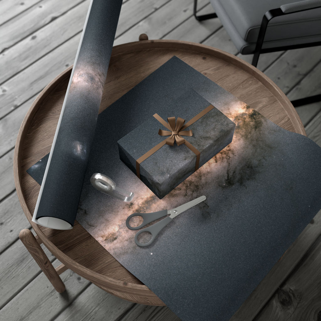Wooden tray with gift wrapping supplies, including a roll of black paper with the galaxy print, a box with a bow, scissors, and a knife on a wooden surface.